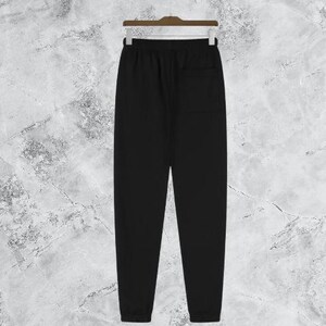 Puede incluir: Pantal&oacute;n de ch&aacute;ndal negro colgado de una percha de madera. El pantal&oacute;n tiene cintura con cord&oacute;n, un bolsillo trasero y pu&ntilde;os el&aacute;sticos en los tobillos. La tela parece ser un material suave y c&oacute;modo.