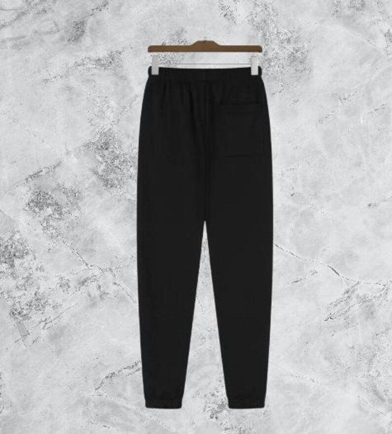 Puede incluir: Pantal&oacute;n de ch&aacute;ndal negro colgado de una percha de madera. El pantal&oacute;n tiene cintura con cord&oacute;n, un bolsillo trasero y pu&ntilde;os el&aacute;sticos en los tobillos. La tela parece ser un material suave y c&oacute;modo.