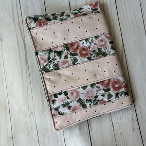 May include: A rectangular book cover with a floral rose pattern and light pink polka dot sections. The cover is made of fabric and has a stitched border. The floral sections feature roses in shades of pink and green.