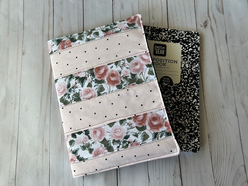 May include: A floral fabric notebook cover with a pink background and black polka dots. The cover features a rose pattern and is next to a composition notebook with the text "POSITION BOOK".