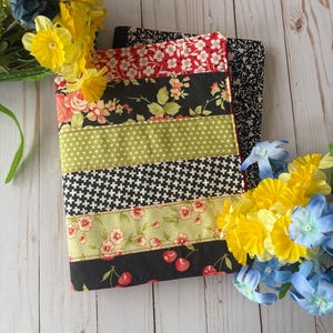 May include: A black and green fabric book cover with a multi-colored striped pattern. The cover features a cherry print, floral print, and polka dot print.