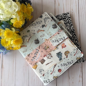 May include: A multi-colored fabric notebook cover with a Harry Potter theme. The cover features a patchwork design with different colored fabrics and illustrations of magical objects, including a wand, a broom, and a snitch. The text "Seeker in Training" and "Wizard in Training" is printed on the cover.