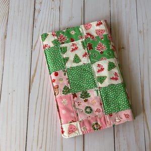 May include: A patchwork Christmas-themed item featuring squares of green polka dots, pink, and white fabric. The fabric is decorated with Christmas trees, gingerbread men, and other holiday motifs. The item is likely a quilted cover or case.
