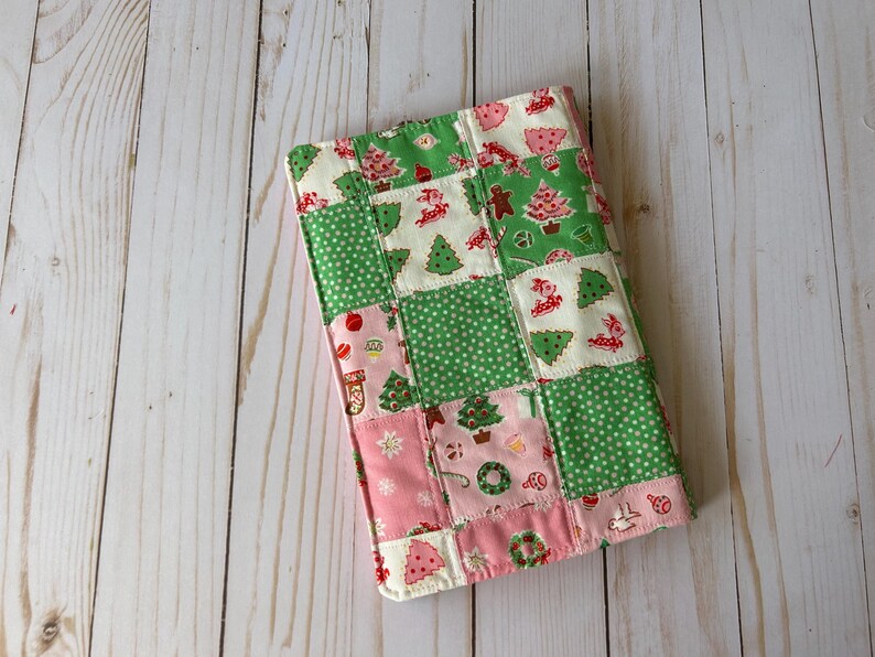 May include: A patchwork Christmas-themed item featuring squares of green polka dots, pink, and white fabric. The fabric is decorated with Christmas trees, gingerbread men, and other holiday motifs. The item is likely a quilted cover or case.