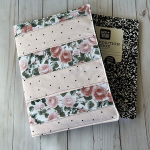 May include: A floral notebook cover with a pink background and black polka dots, paired with a composition notebook. The cover features rose patterns and is stitched with black thread. The composition notebook has a black and white speckled design.