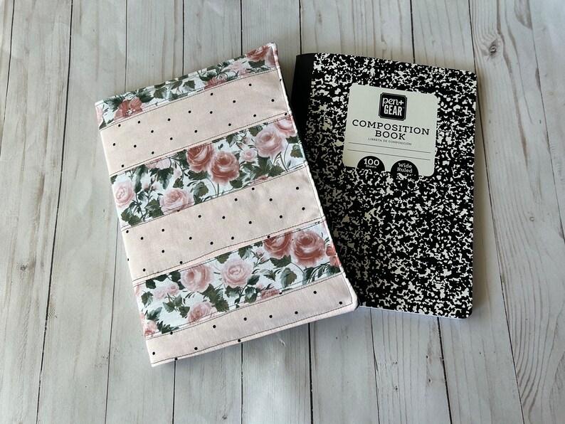 May include: A floral notebook cover with a pink background and black polka dots, paired with a black and white composition book. The cover features rose patterns and the text "Pen+Gear Composition Book".