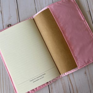 May include: Open pink journal with lined pages and a brown cover. The journal is in a pink satin cover. The text "Thanks for choosing Feela www.feela-us.com" is printed at the bottom of the page.