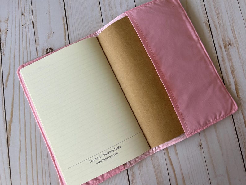 May include: Open pink journal with lined pages and a brown cover. The journal is in a pink satin cover. The text "Thanks for choosing Feela www.feela-us.com" is printed at the bottom of the page.