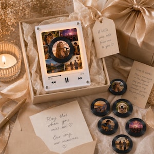 Puede incluir: Un reproductor de m&uacute;sica blanco con un disco negro en el centro, rodeado de fotos. El reproductor est&aacute; en una caja de regalo con un lazo e incluye peque&ntilde;os discos con fotos. El texto en el reproductor dice "05:20" y "13:14".
