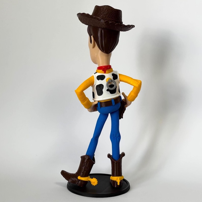 May include: A plastic figurine of a cowboy character wearing a brown hat, a white vest with black cow-print spots, a red neckerchief, yellow long sleeves, blue pants, and brown boots with yellow spurs. A pull-string ring is visible on the back.
