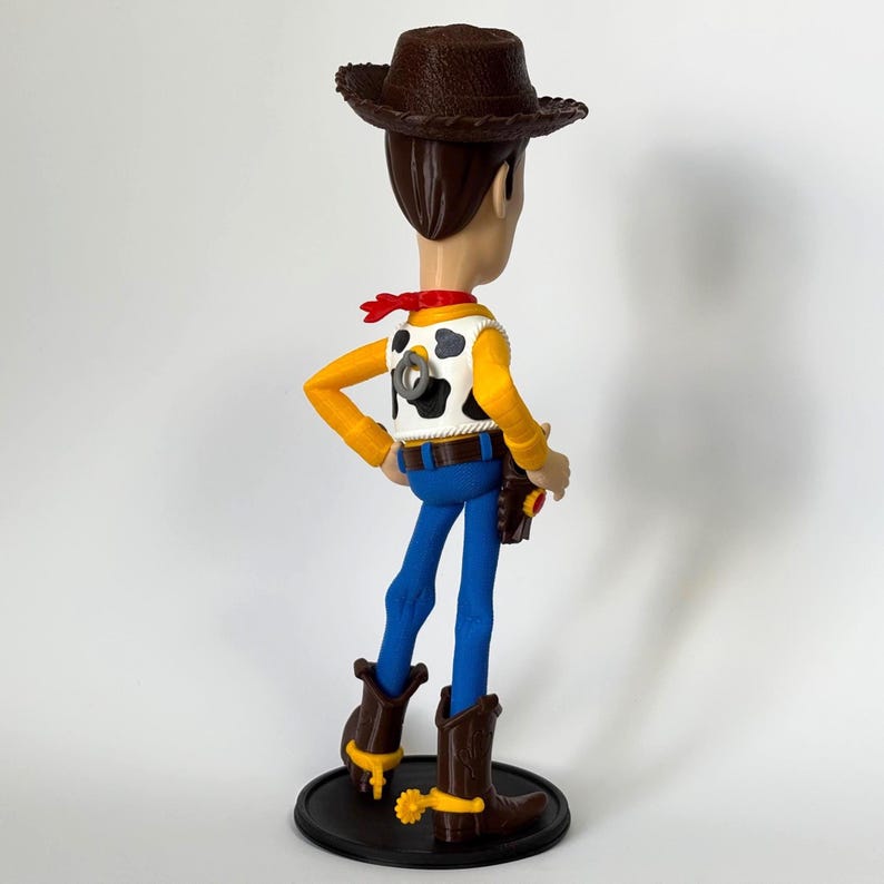 May include: A standing cowboy figurine featuring a brown cowboy hat, a white vest with black cow-print spots, a red neckerchief, blue pants, and brown boots with yellow spurs. A grey pull-string ring is visible on the back of the vest.