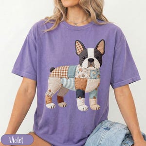 Op de afbeelding: Een violetkleurig T-shirt met korte mouwen en een afbeelding van een Franse Bulldog in patchworkstijl. De illustratie van de hond bevat diverse stoftexturen, waaronder bruine ruiten, bloemenprints en strepen, afgewerkt met kleine bruine knoopjes.