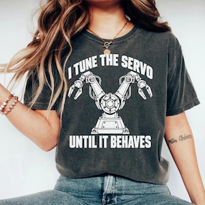 Könnte beinhalten: Ein anthrazitfarbenes Kurzarm-T-Shirt mit einer weißen Grafik eines Roboterarms mit zwei Greifern. Der Text über der Grafik lautet I TUNE THE SERVO und der Text unter der Grafik lautet UNTIL IT BEHAVES in einer fetten, serifenlosen Schrift.