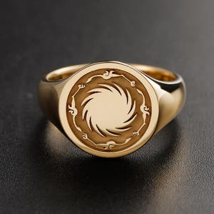 Könnte beinhalten: Ein goldener Siegelring mit einer kreisförmigen Platte in polierter Ausführung. Die Mitte des Rings zeigt ein eingraviertes Spiral-Sonnenstrahlenmuster, das von einer dekorativen Bordüre aus kleinen, stilisierten wolkenartigen Motiven umgeben ist.