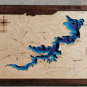 May include: Wooden map of Starvation Reservoir in Duchesne, Utah, with a dark brown frame. The map features a layered blue and light blue depiction of the lake's depth, with roads and a compass rose. The text "Starvation Reservoir" is carved at the top.