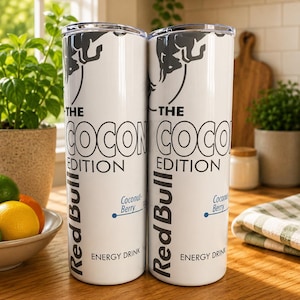 Pode incluir: Dois copos cil&iacute;ndricos brancos com o log&oacute;tipo da Red Bull e o texto THE COCONUT EDITION, Coconut Berry e ENERGY DRINK. O design inclui um gr&aacute;fico de um touro cinzento escuro no topo e detalhes azuis sobre um fundo branco limpo.