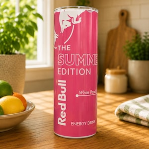Pode incluir: Um copo cil&iacute;ndrico com um exterior rosa brilhante com gr&aacute;ficos e texto em branco. O design inclui o log&oacute;tipo da Red Bull, o texto THE SUMMER EDITION, o r&oacute;tulo de sabor White Peach e as palavras ENERGY DRINK.