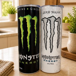 K&ouml;nnte beinhalten: Zwei zylindrische Trinkbecher mit durchsichtigen Deckeln. Der linke Becher ist schwarz mit einem hellgr&uuml;nen Krallen-Logo sowie dem Text "Monster Energy" und "Taurine + Ginseng". Der rechte Becher ist wei&szlig; mit einem grauen Krallen-Logo und dem Text "Zero Sugar" und "Monster Energy Ultra".