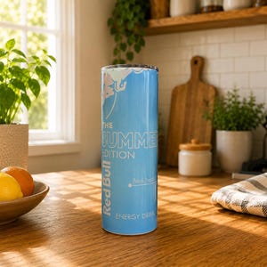 Pode incluir: Um copo cil&iacute;ndrico azul-claro com o log&oacute;tipo Red Bull The Summer Edition em texto branco. O design inclui um gr&aacute;fico de flores brancas no topo e as palavras Energy Drink na parte inferior, com um acabamento liso e um rebordo met&aacute;lico plano.