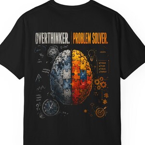 Könnte beinhalten: Ein schwarzes T-Shirt mit einem Grafikdruck auf der Rückseite. Das Motiv zeigt ein Gehirn, das in eine blaue und eine orangefarbene Puzzlehälfte geteilt ist. Der Text lautet OVERTHINKER und PROBLEM SOLVER, ergänzt durch Symbole wie Uhr, Zahnräder und Zielscheibe.