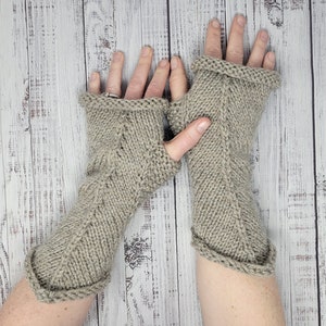May include: A pair of light beige fingerless gloves crafted from a chunky knit yarn. The gloves feature a vertical ribbed pattern running along the center and rolled edges at both the top and bottom openings, providing a textured appearance.