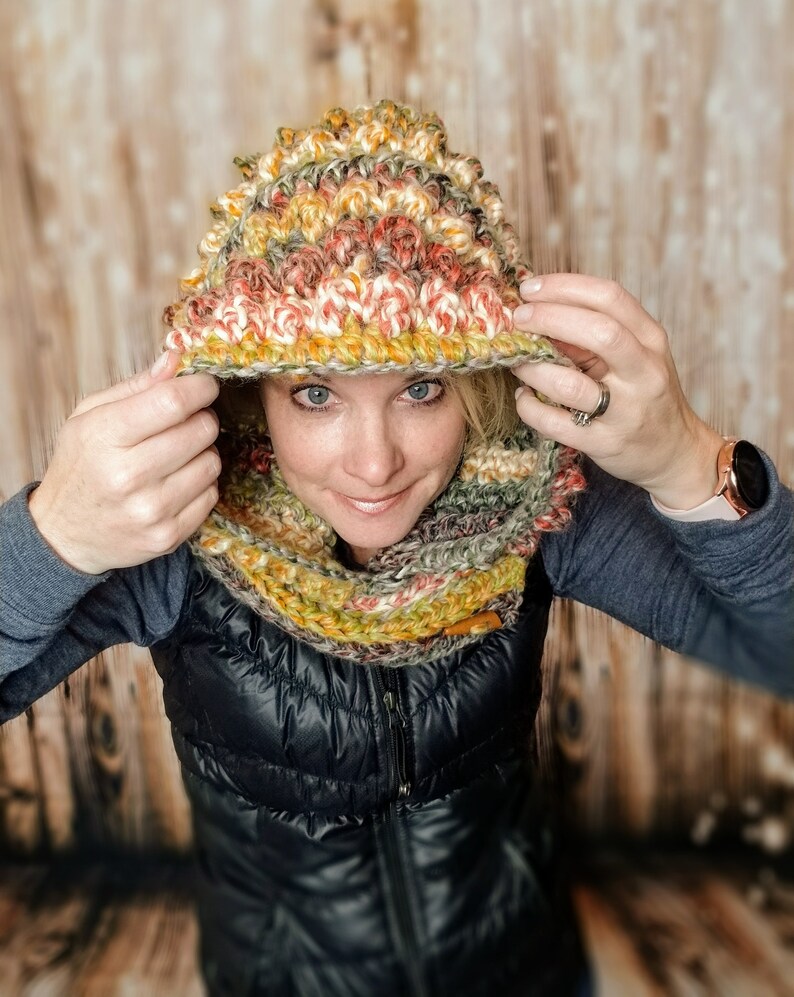 May include: A multi-colored crocheted hooded scarf with a textured pattern. The scarf is made with shades of green, brown, orange, and white yarn.