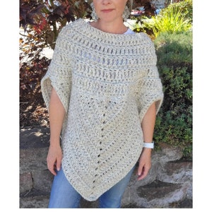 May include: A crocheted poncho in a light beige colour with a textured pattern. The poncho has a wide neckline and a loose fit.