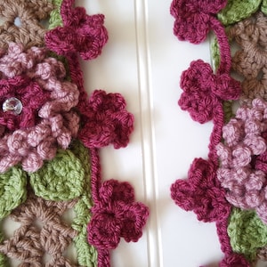 Pode incluir: Close-up de uma guarnição de crochê com flores bordô, marrom e verde. Cada flor tem um strass brilhante no centro.