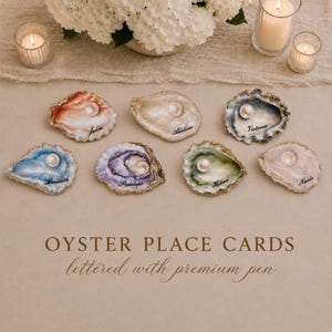 May include: Seven oyster shells arranged on a surface, each featuring a unique interior color including orange, blue, purple, green, and white. Each shell contains a single white pearl and is personalized with a name written in black ink.