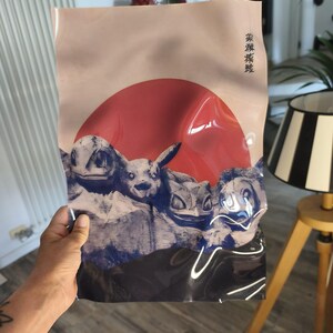 Può includere: Un sacchetto di plastica rettangolare con una stampa grafica di quattro creature stilizzate in toni di blu e bianco su un grande cerchio rosso. Il design include caratteri giapponesi nell'angolo in alto a destra su uno sfondo beige chiaro.