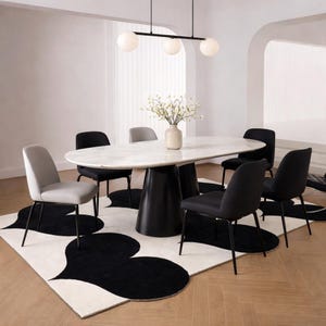 May include: A contemporary dining set. An oval marble-effect table with a black base is surrounded by six chairs, some grey, some black. A black and white patterned rug lies beneath. A light fixture with three globe lights hangs above the table.