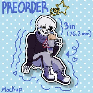May include: A 3-inch (76.2 mm) keychain mockup featuring a cartoon skeleton character holding a cup with a small animal inside. The keychain has a gold star charm and the word "PREORDER" is written at the top. The background is light blue with white polka dots.