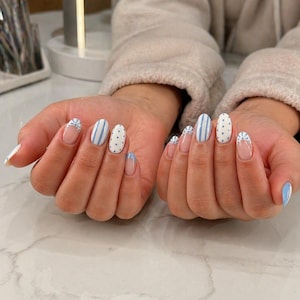 May include: Manicured nails with a light blue and white design. Some nails feature blue stripes, polka dots, or a delicate lace pattern. The nails are oval-shaped with a clear base and blue tips.