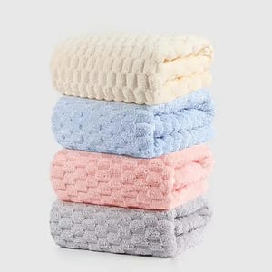May include: Four folded towels in a stack, in cream, pale blue, pink, and grey. Each towel has a textured, quilted design. The towels are neatly arranged, one on top of the other, creating a tidy and organised display.