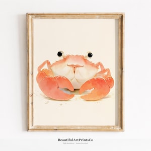 May include: A framed wall art print featuring a watercolour illustration of a light orange crab with large black eyes and prominent claws, centred on a cream-coloured background. The wooden frame has a weathered, light brown finish.