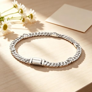 May include: A silver-toned chain link bracelet featuring a rectangular clasp engraved with the word PANDORA. The bracelet is accented with four small, heart-shaped clear stones integrated into the chain links at regular intervals.
