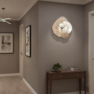 May include: A wall clock with a unique design, featuring a light-colored, abstract shape with a circular clock face. The clock has black hands and numbers, and is mounted on a gray wall. The clock is approximately 12 inches in diameter.