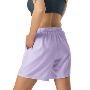 May include: Light purple athletic shorts featuring an elastic waistband and side pockets. The shorts have a relaxed fit and a smooth, solid-colored fabric construction, extending to the mid-thigh with a clean, straight hemline design.