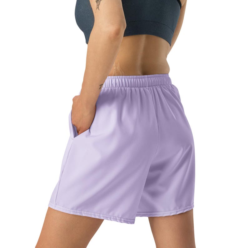 May include: Light purple athletic shorts featuring an elastic waistband and side pockets. The shorts have a relaxed fit and a smooth, solid-colored fabric construction, extending to the mid-thigh with a clean, straight hemline design.