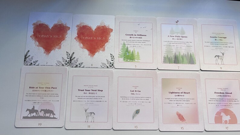 May include: A collection of ten rectangular oracle cards arranged in two rows. The cards feature various illustrations including red watercolour hearts, green pine trees, a deer, a feather, and horses, alongside English and Japanese text titles.