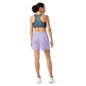 May include: A racerback sports bra in a dark grey heathered fabric with black trim paired with solid light purple athletic shorts featuring an elastic waistband and white sneakers, shown from a rear perspective against a plain white background.