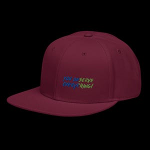 May include: A maroon baseball cap with a flat brim and embroidered text on the front that reads YOU DESERVE EVERYTHING! in alternating blue and green letters. The cap features a structured crown with a top button and stitched eyelets.