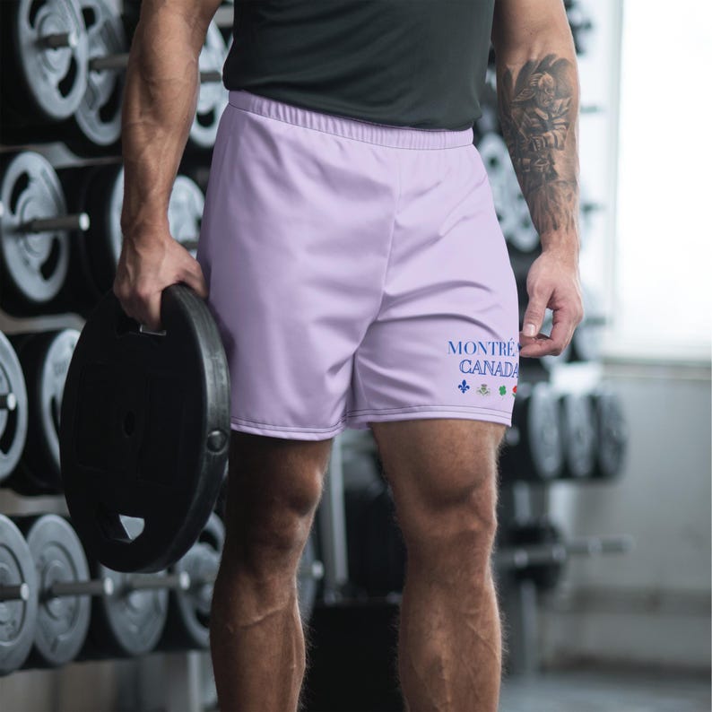 May include: Light purple athletic shorts featuring the text MONTR&Eacute;AL CANADA in blue lettering on the lower left leg, accompanied by a small blue fleur-de-lis symbol and three additional small colorful icons arranged in a horizontal row.