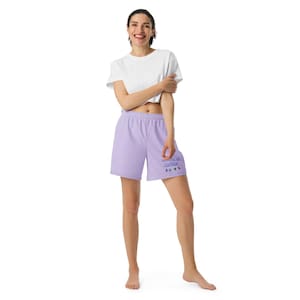 May include: A white short-sleeved crew neck t-shirt paired with lavender athletic shorts. The shorts feature the text "MONTREAL CANADA" in blue lettering on the lower left leg, accompanied by small, colorful graphic icons of a maple leaf and flowers.