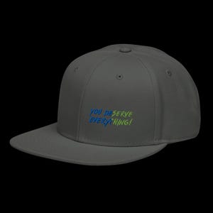 May include: A charcoal grey baseball cap with a flat brim and an embroidered design on the front. The text reads YOU DESERVE EVERYTHING! in a stylised font, with the word YOU DESERVE in blue and EVERYTHING! in a bright lime green colour.