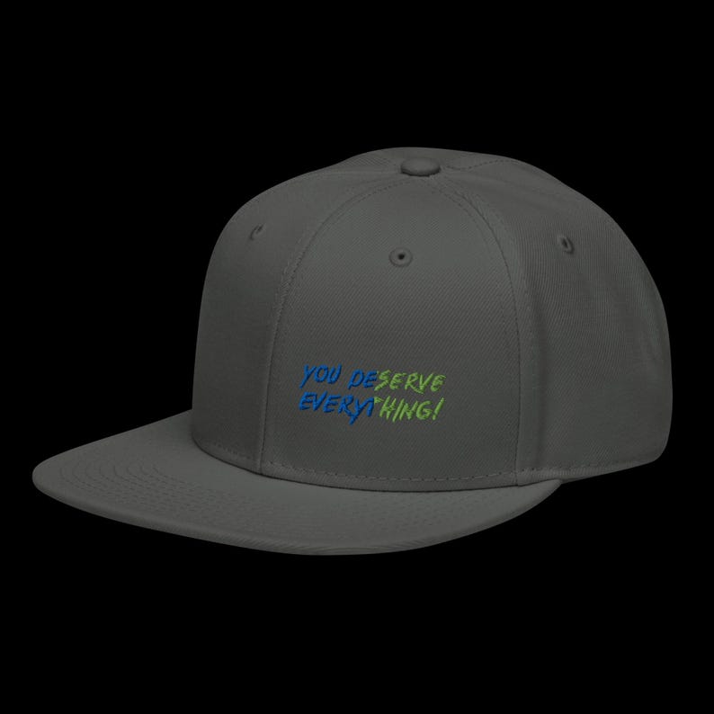 May include: A charcoal grey baseball cap with a flat brim and an embroidered design on the front. The text reads YOU DESERVE EVERYTHING! in a stylised font, with the word YOU DESERVE in blue and EVERYTHING! in a bright lime green colour.