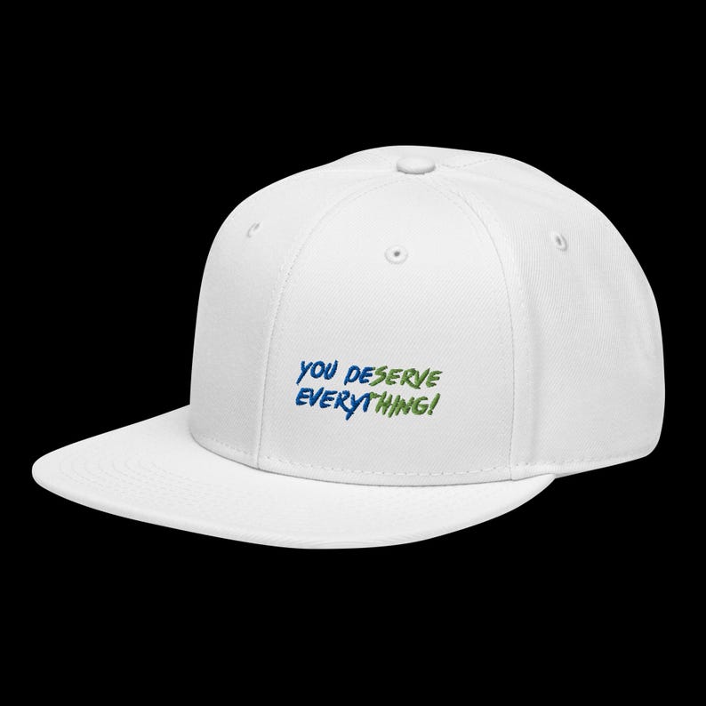 May include: A white baseball cap with a flat brim and a structured crown. The front of the cap features embroidered text in blue and green that reads, "YOU DESERVE EVERYTHING!" The cap includes a top button and ventilation eyelets on the panels.