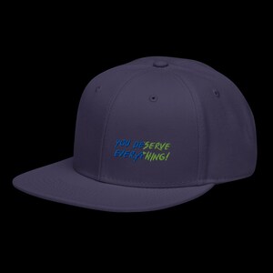 May include: A dark purple baseball cap with a flat brim and a structured crown. The front features embroidered text that reads YOU DESERVE EVERYTHING! in a split colour design, with the first half in blue and the second half in lime green.