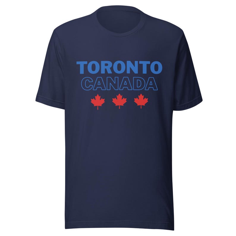 Op de afbeelding: Een marineblauw t-shirt met korte mouwen voorzien van de tekst TORONTO in effen blauwe letters boven het woord CANADA in een blauw omlijnd lettertype. Onder de tekst staan drie rode esdoornblad-iconen horizontaal op de borst.