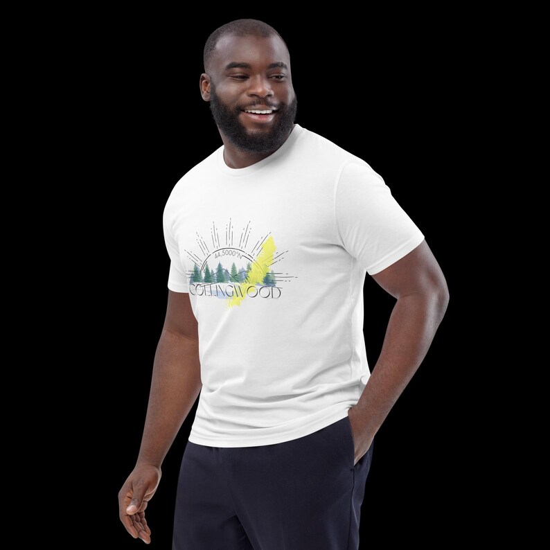 Pode incluir: Uma t-shirt branca de manga curta com uma impress&atilde;o gr&aacute;fica de uma paisagem florestal com um raio amarelo, linhas de sol e o texto COLLINGWOOD com as coordenadas 44.5000&deg;N impressas em tinta preta no centro do peito.